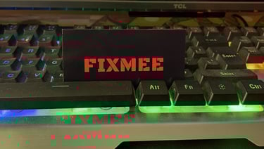 A FIXMEE business card placed on an RGB backlit gaming keyboard with green and blue LED lights.