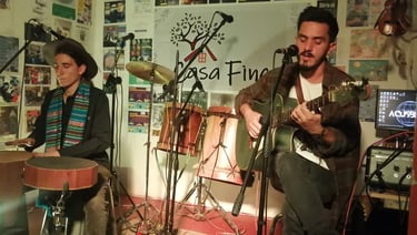 Dos músicos interpretando música folclórica en vivo con una guitarra acústica y un tambor de mano 
