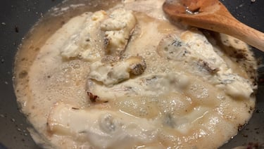 Gorgonzola cheese melting into a creamy white sauce in a skillet with a wooden spoon.
