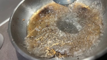 Deglazing a stainless steel pan with liquid to make a flavorful pan sauce.