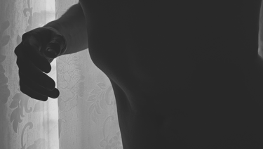 Silueta de torso y mano masculina en blanco y negro frente a cortina.