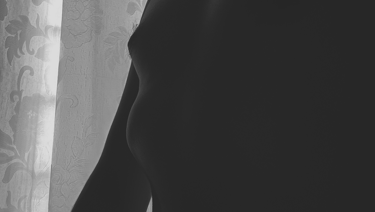 Silueta de pecho y torso masculino en blanco y negro ante cortina.