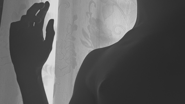 Siluetas desnuda de una mano y un torso contra una cortina.