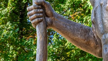 Close-up of Saint Christopher’s hand gripping a wooden staff, symbolizing pilgrimage and sanctuary.