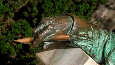 Close-up of Anonymous’s hand holding a quill pen in Miklós Ligeti’s 1903 statue.