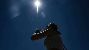 Silhueta de uma pessoa bebendo água sob o sol forte em um dia de calor.