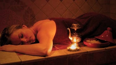Une femme allongée sur une table de Hammam profitant d'un moment de détente en fermant les yeux.