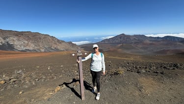 Woman standing by trail sign at Haleakalā crater wearing hiking outfit