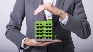 Business professional protecting a green apartment building model representing real estate insurance concepts.