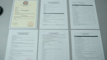 Overhead flat-lay of regulatory certificates, certificates of analysis, and compliance documents spread on a gray desk surface under cool daylight, batch codes visible, precise clinical arrangement