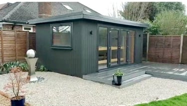 Modern dark grey insulated garden office with glass doors and composite decking