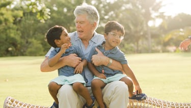 grandfather sitting and hugging his grandchildren on a woven chair at rimba by ayana bali during relaxed family photography