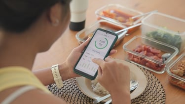 A woman using a calorie counter app on her smartphone to track nutrition during meal prep.