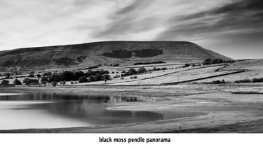 a black and white photo of pendle hill reflected in the waters of black moss reservoir