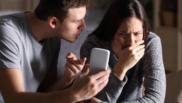 a man and woman sitting on a couch looking at a cell phone