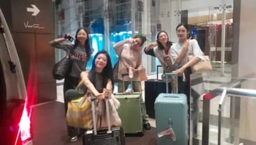 Lima orang perempuan berpose ceria di depan pintu kaca membawa koper masing-masing.