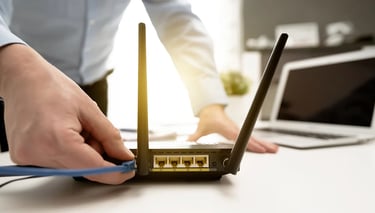 A person connecting a blue ethernet cable into a wireless WiFi router for home internet setup.