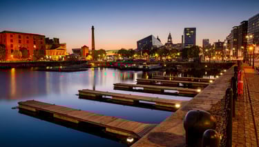 Liverpool's Royal Albert Dock at sunset with empty wooden piers and city skyline lights.