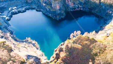 Aerial view of a heart-shaped blue lake surrounded by rocky quarry cliffs 