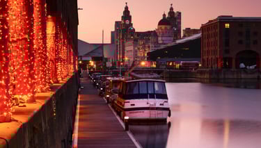 Royal Albert Dock Liverpool at sunset with festive lights, boats, and the Liver Building skyline.