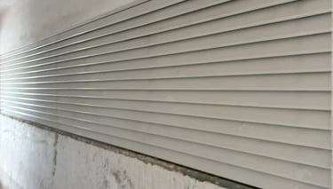 Close-up of a white metal rolling shutter door installed on a weathered concrete wall in an industrial setting.