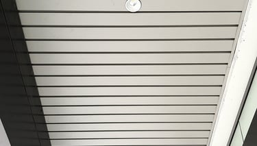 Low angle view of a modern slatted metal ceiling with an integrated LED recessed light fixture.