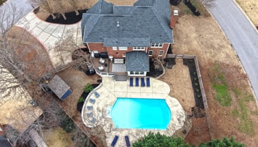 Drone Aerial view of a luxury brick home featuring a backyard swimming pool and stone patio.