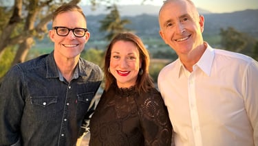 Three smiling professional colleagues posing outdoors at sunset with scenic mountain views.