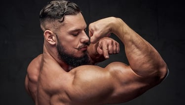 A muscular man with a groomed beard and mustache flexing his large bicep and back muscles.