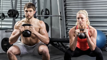 A fit man and woman performing kettlebell goblet squats during a strength training workout at the gym.