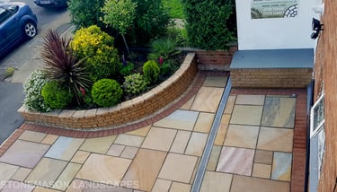 Colourful sandstone paving driveway and curved raised planter with colourful plants and flowers
