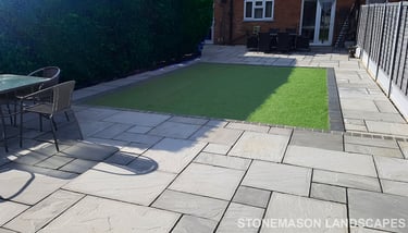 Fully paved grey sandstone patio with charcoal edging bocks and artificial grass lawn