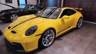 a yellow Porsche 911 GT3 parked in a garage next to a 1989 Porsche 911 Carrera awaiting appraisal