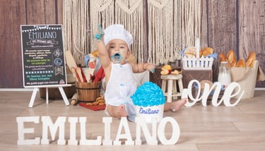 a baby boy in a white dress and a cake