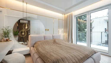 Jasna sypialnia z tapicerowanym łóżkiem, okrągłym lustrem, lampami wiszącymi i balkonem.