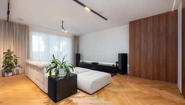 Nowoczesny salon z jasną sofą, drewnianą podłogą, zasłonami i niską szafką RTV.