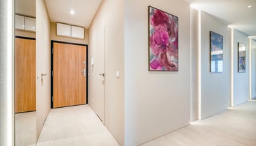 Jasny korytarz z drzwiami wejściowymi z drewna, lustrzaną szafą po lewej oraz obrazami na ścianach