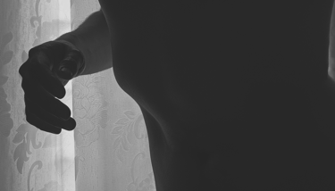 Silueta desnuda de un torso y una mano frente a una cortina con flores.