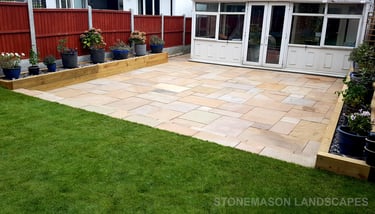 Large sandstone patio and raised wooden sleeper planters