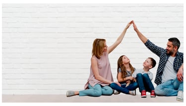 A happy family creates a roof shape with their hands in front of a white brick wall, symbolizing home security.