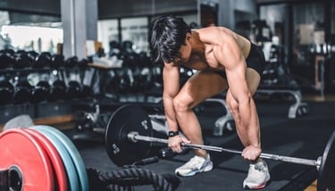 Muscular man performing a heavy barbell deadlift for strength training in a modern fitness gym.