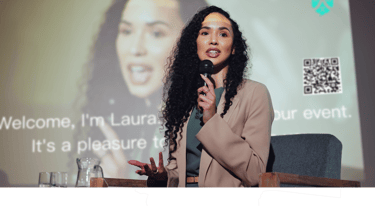 a woman in a suit and a microphone in front of a screen with Ohaio LIvesSpeaker working