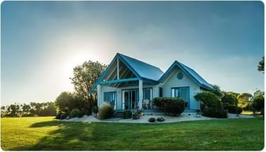 Modern blue beach cottage with a large green lawn and garden landscape under a sunny sky.