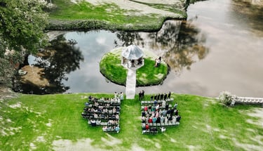 Drone photo of an outdoor wedding ceremony by a lakeside gazebo surrounded by guests