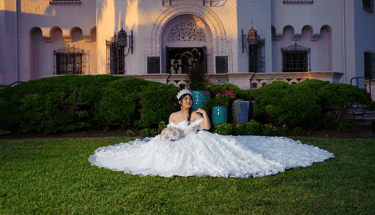 a woman in a wedding dress sitting posing for photographer on a lawn