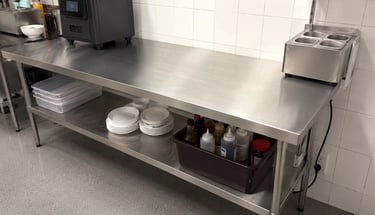 Long stainless steel benches for commercial kitchens holding plates and condiments.