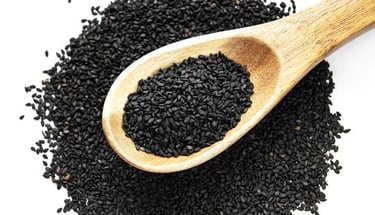 a wooden spoon with black sesame seeds and some of seeds on the ground
