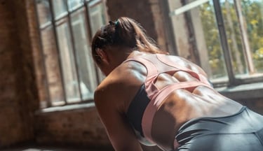 Sweaty back of a fit woman in a sports bra performing a workout routine in a bright gym studio.