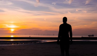 Silhouette of Antony Gormley's Another Place iron man statue on Crosby Beach during a golden sunset.