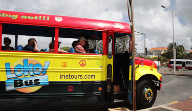 Ônibus turístico colorido circulando pelas ruas de Willemstad, Curaçao, oferecendo passeios.